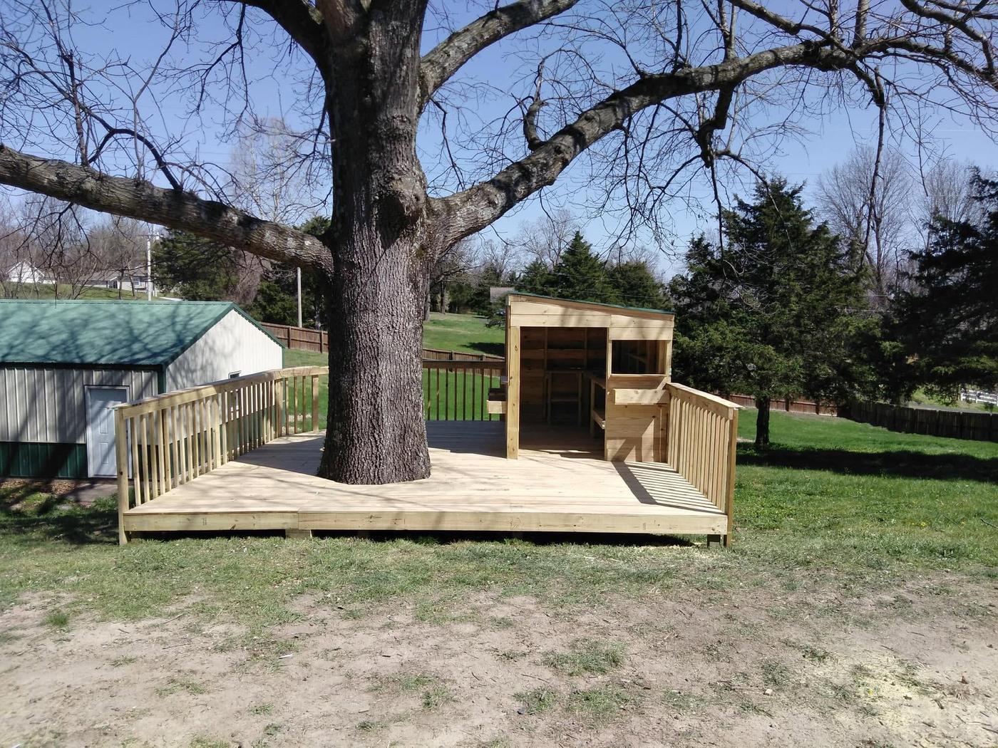A timber deck built to wrap around a mature tree, with railings and a small cedar structure at one end